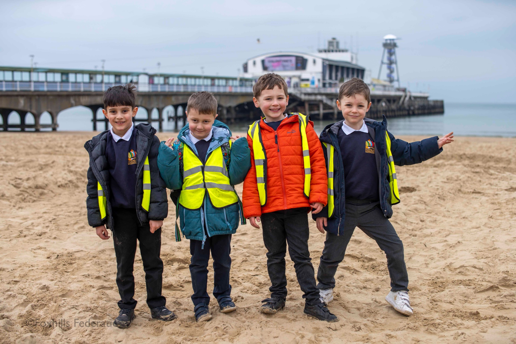 A group of children smile and pose in front of Bournemouth pier.