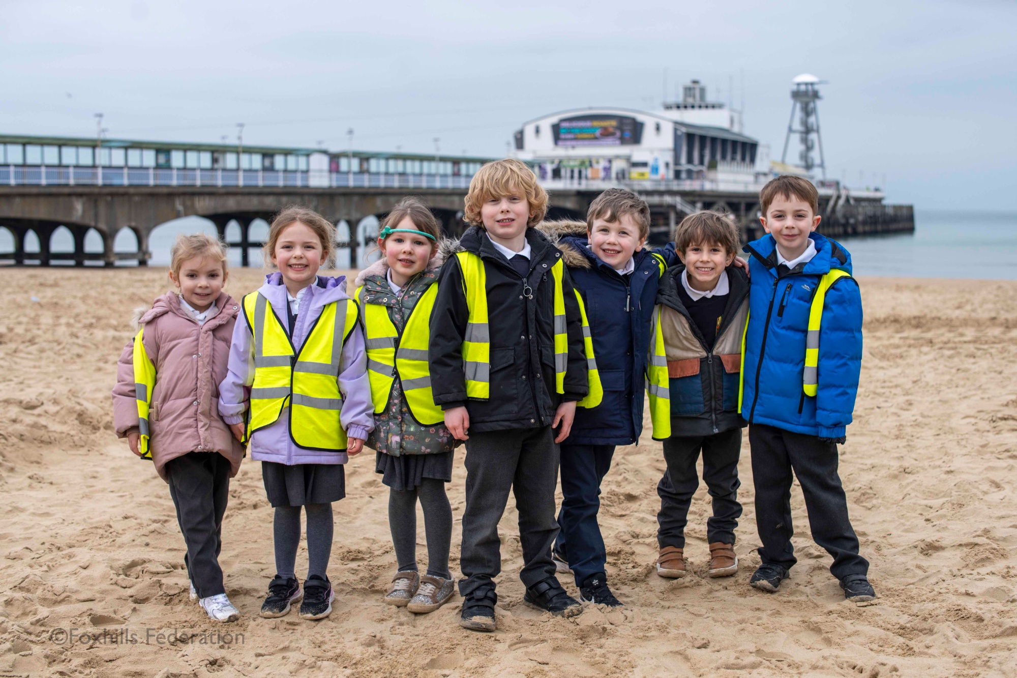 A group of children smile and pose in front of Bournemouth pier.