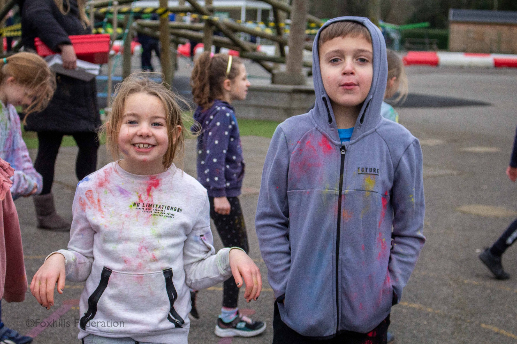 Two children stand covered in paint